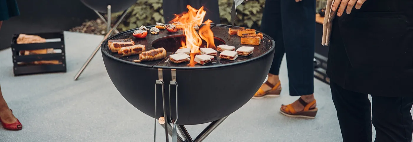 Höfats BOWL fire pit with plancha and grate cooking food during a reception
