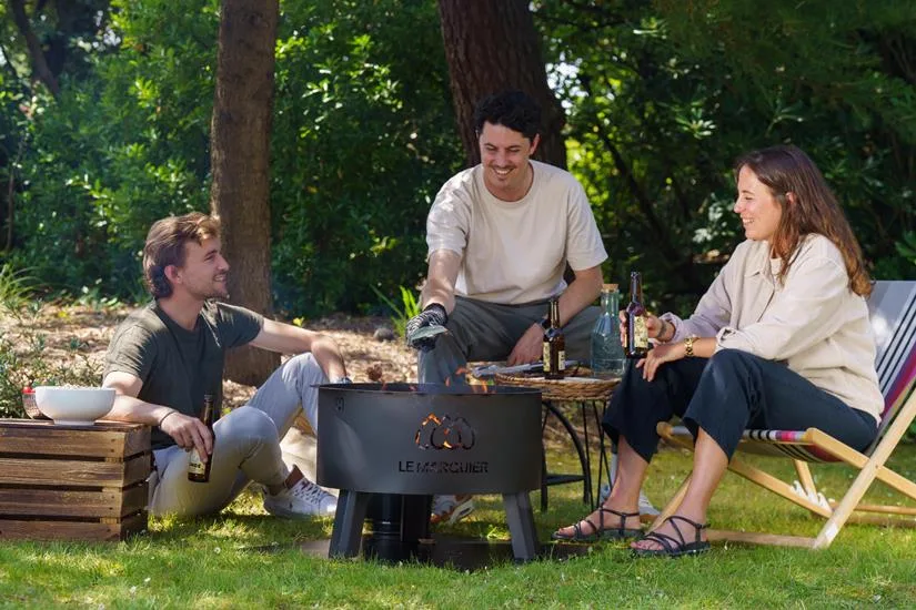 Le Marquier Original black fire pit in a garden setting with its cooking grate
